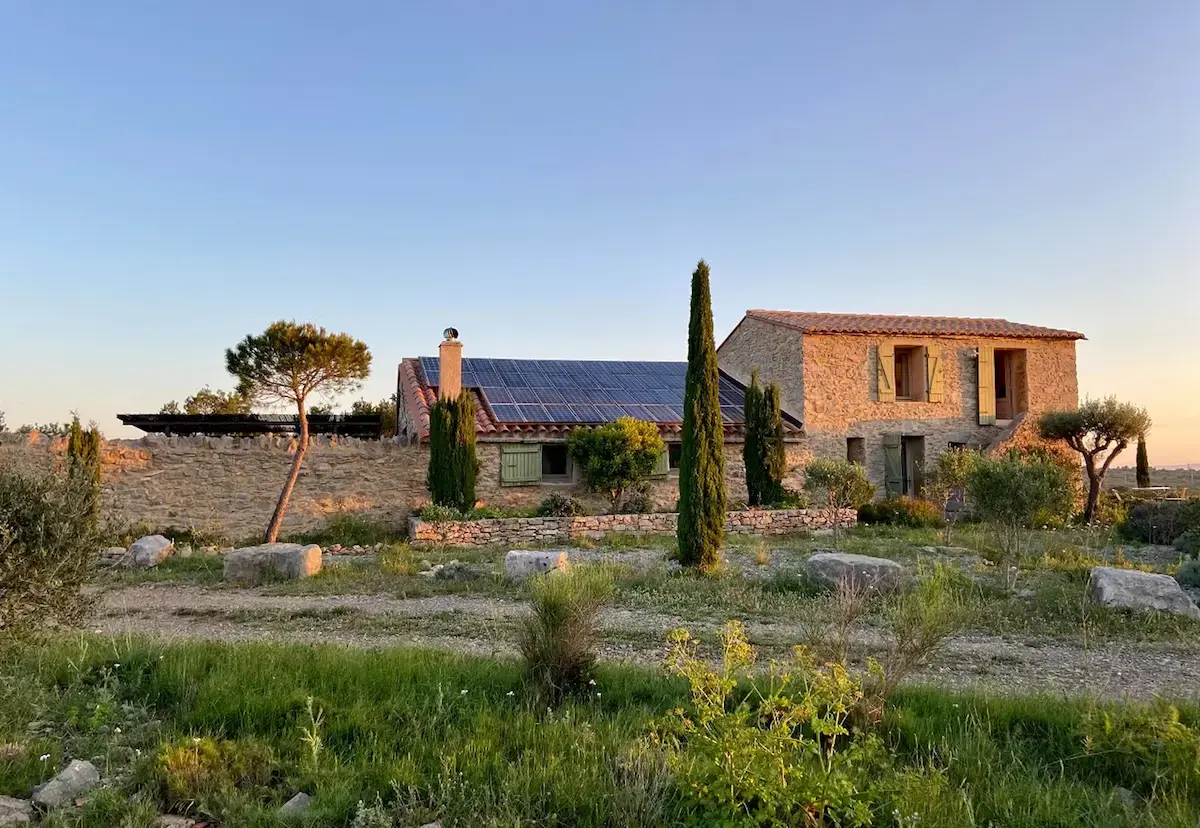 GreenGo - Maison en pierre avec panneaux solaires au coucher du soleil.