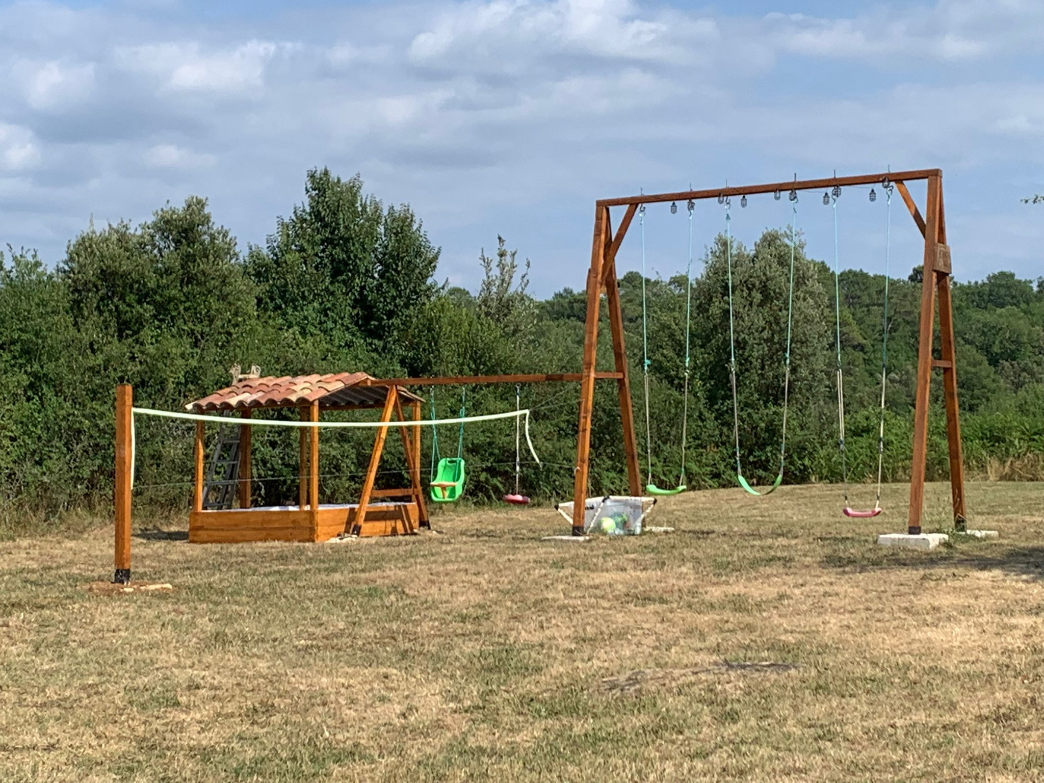 Grand terrain de jeu avec balançoires hautes, un bac à sable et un filet de volley-ball/badminton.